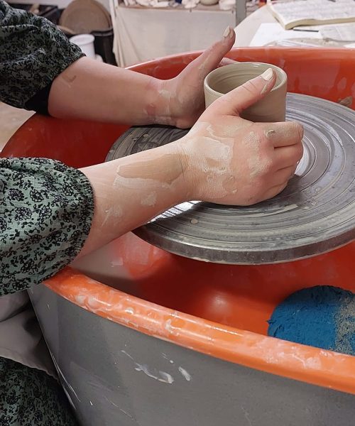 Student shaping pottery on the wheel at Clay Magic studio.