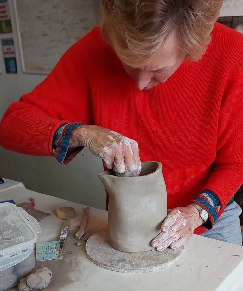 Woman shaping a vase with clay at Clay Magic pottery studio.